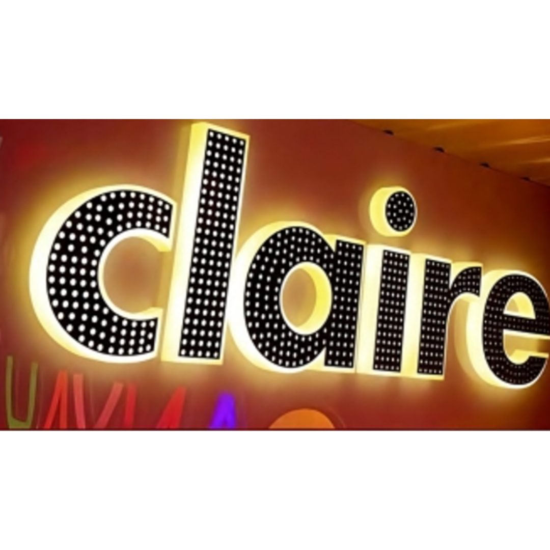 Close-up of illuminated raised lettering spelling “claire,” with black dotted interiors, bright white edges, and a warm yellow glow against a reddish background.