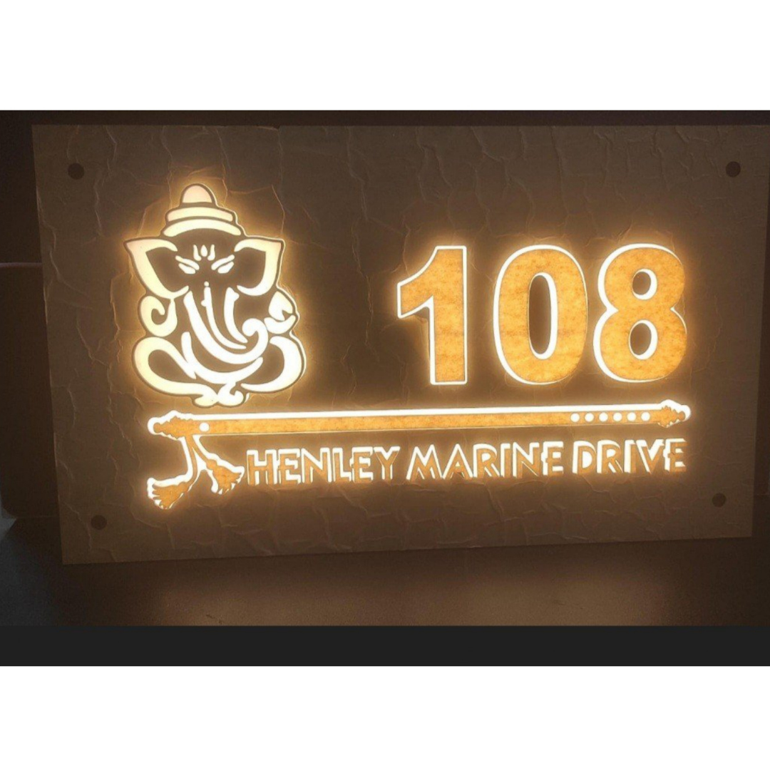Glowing wall-mounted name plate featuring a Ganesha symbol, the number 108, and the text “HENLEY MARINE DRIVE”