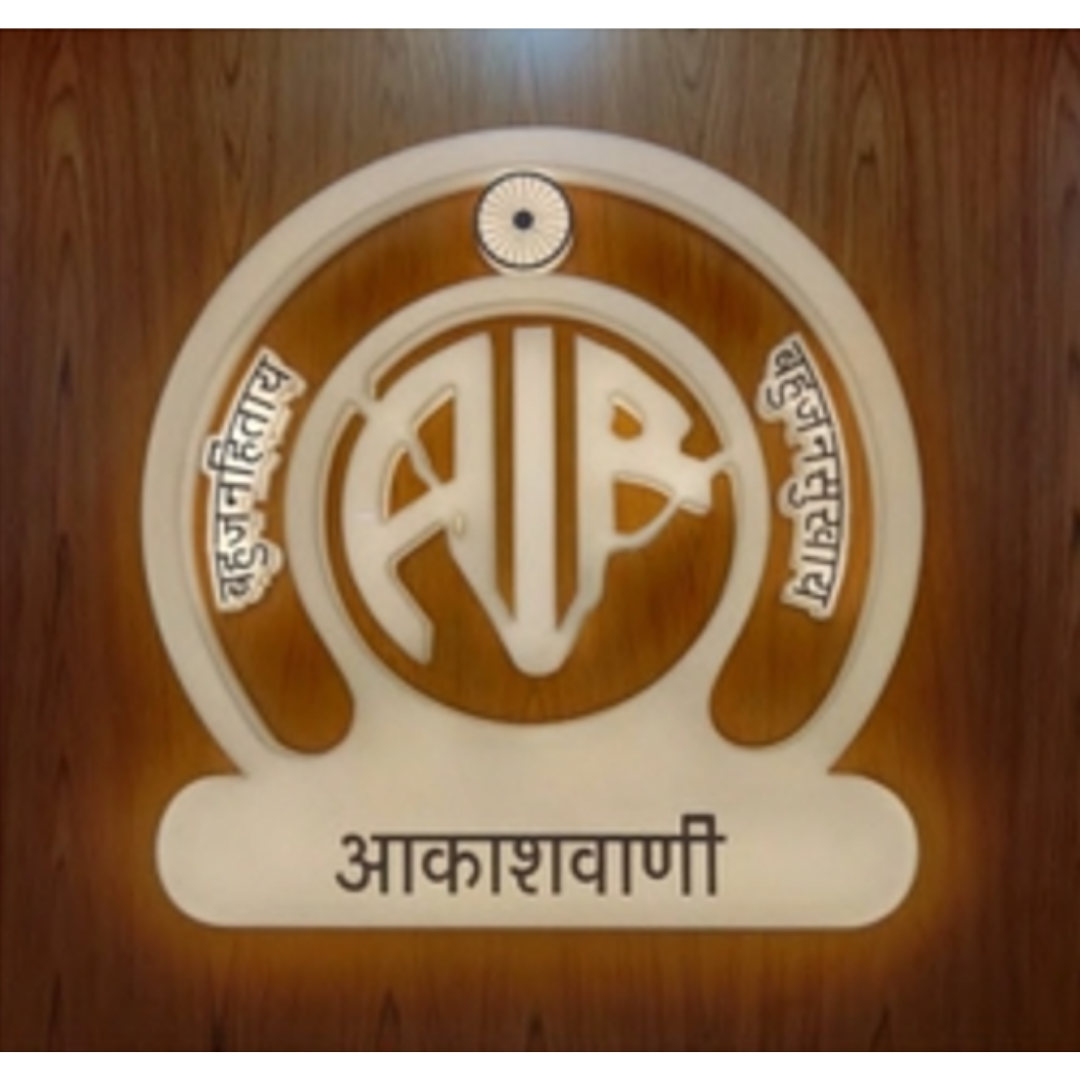 A circular decorative sign featuring the Akashvani logo and Hindi text, mounted on a wooden background.