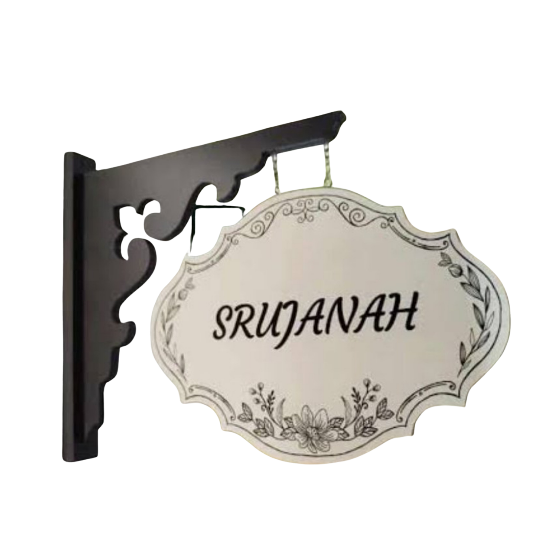 Decorative cream-colored hanging name plate reading “SRUJANA,” suspended from an ornate black wall bracket.