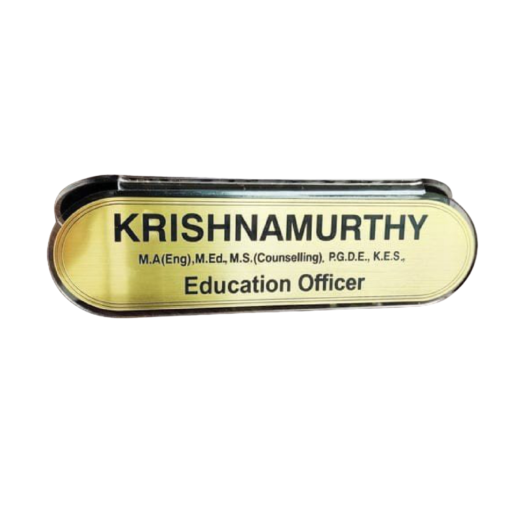 Gold-colored oval-edged name plate reading “KRISHNAMURTHY” with educational qualifications and the designation “Education Officer.”