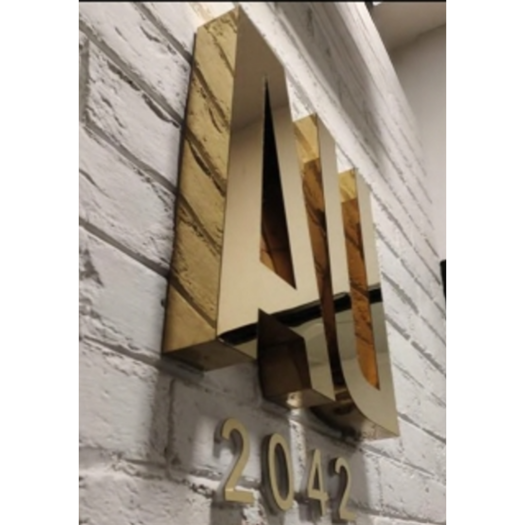 Large reflective gold three-dimensional lettering and the number “2042” mounted on a white brick wall.
