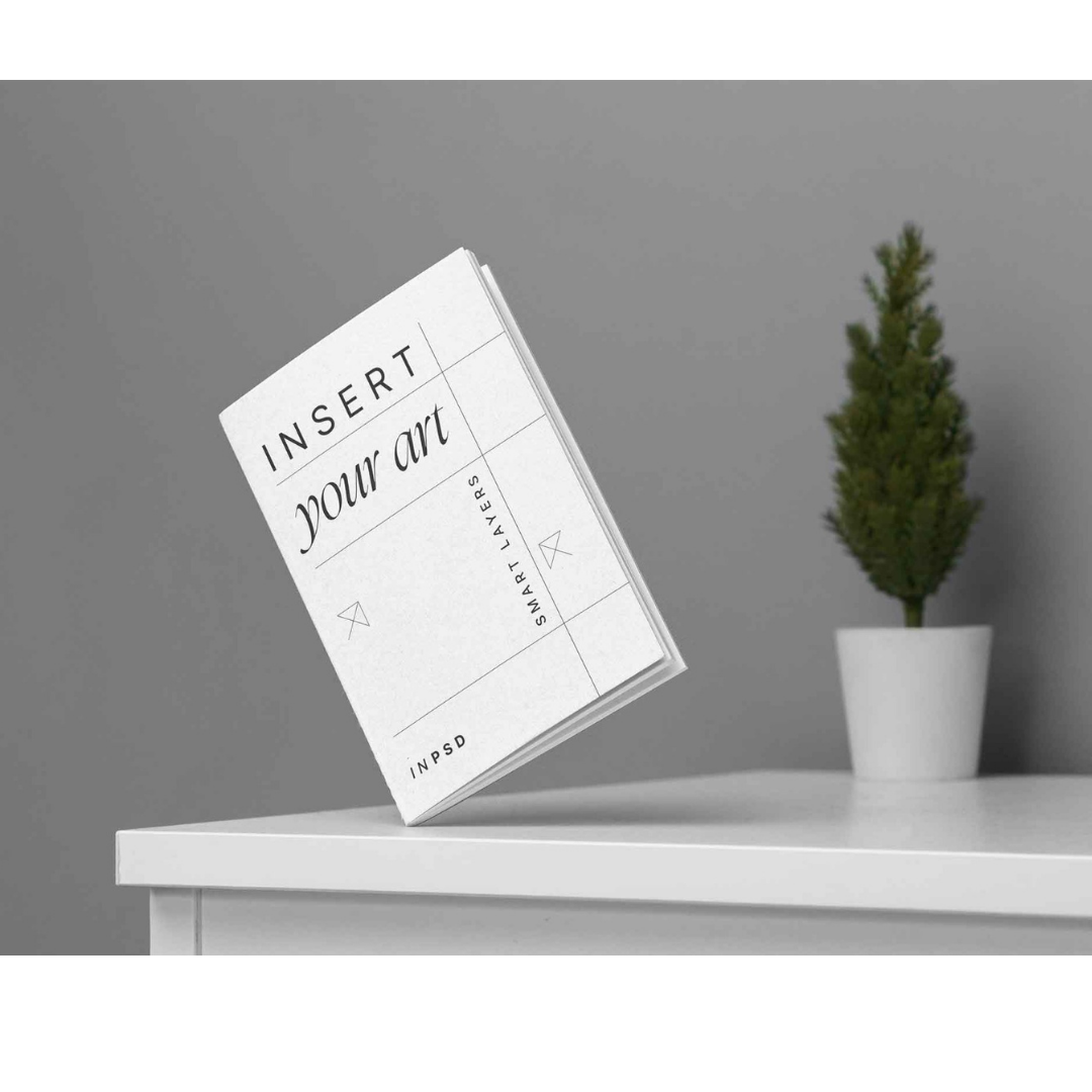 Minimal white brochure mockup standing on a table beside a potted plant