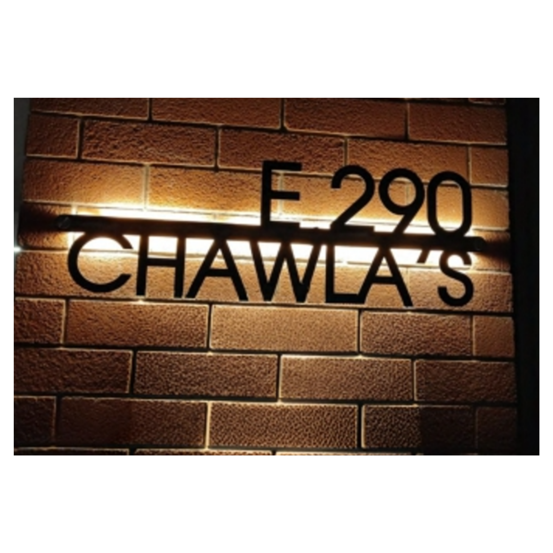 Modern black metal nameplate displaying “E-290” and “CHAWLA’S” with warm backlighting against a brick wall.